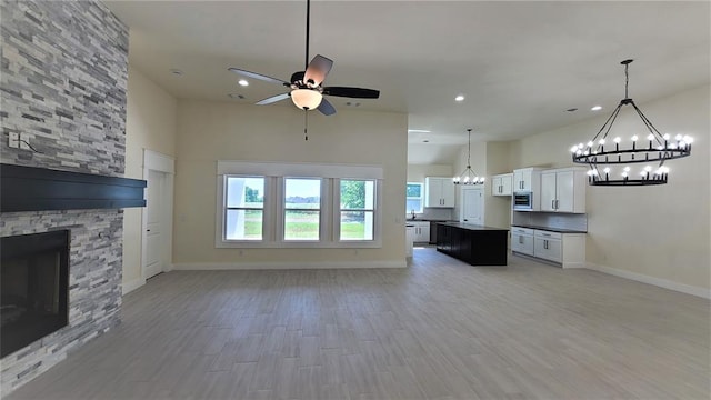 unfurnished living room featuring a towering ceiling, ceiling fan, sink, light hardwood / wood-style flooring, and a fireplace