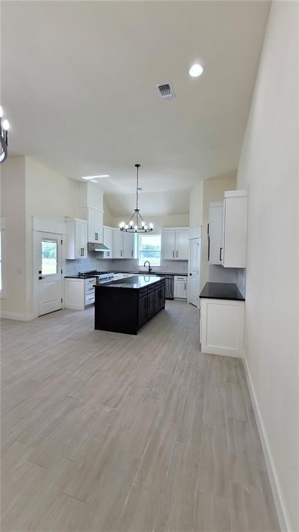 108 Tralee Ct, Yukon, OK 73099 - kitchen with a chandelier, a kitchen island with sink, baseboards, dark countertops, and exhaust hood