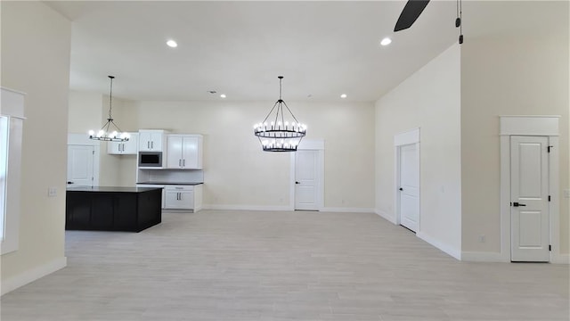 kitchen with ceiling fan with notable chandelier, a kitchen island, a high ceiling, white cabinetry, and stainless steel microwave