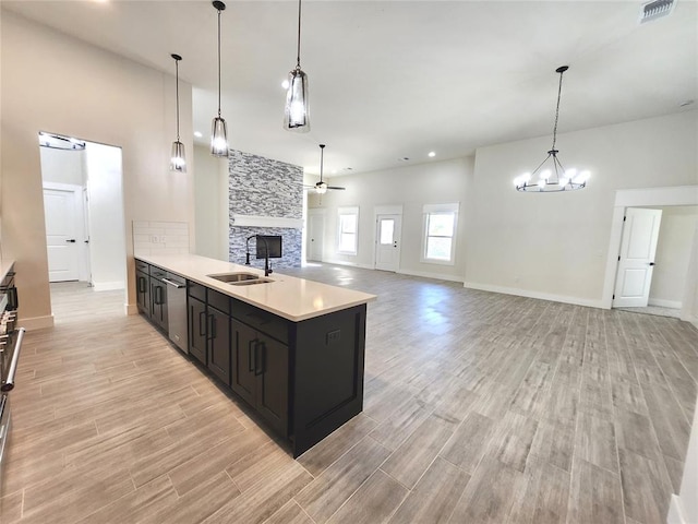 kitchen featuring ceiling fan with notable chandelier, sink, hanging light fixtures, stainless steel dishwasher, and light wood-type flooring