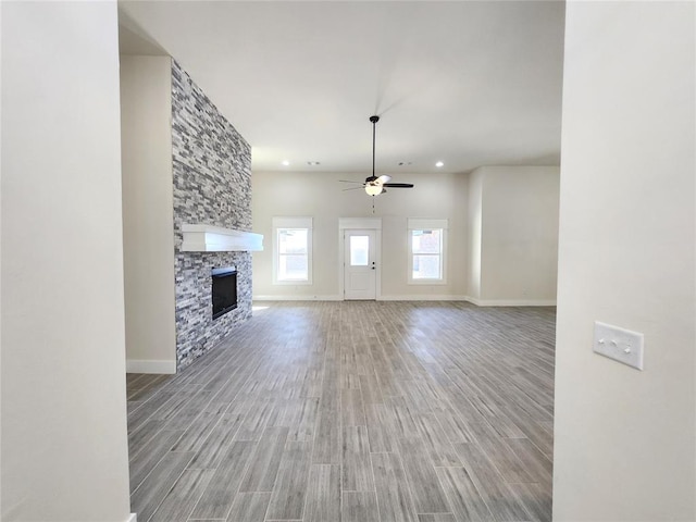 unfurnished living room featuring a stone fireplace, ceiling fan, and wood-type flooring