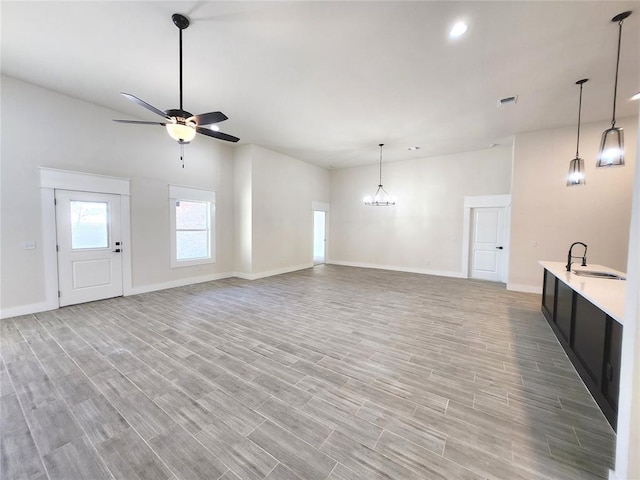 unfurnished living room featuring light hardwood / wood-style flooring, ceiling fan with notable chandelier, and sink