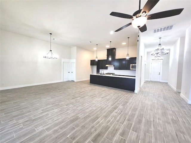 kitchen featuring pendant lighting, a kitchen island with sink, exhaust hood, ceiling fan with notable chandelier, and hardwood / wood-style flooring