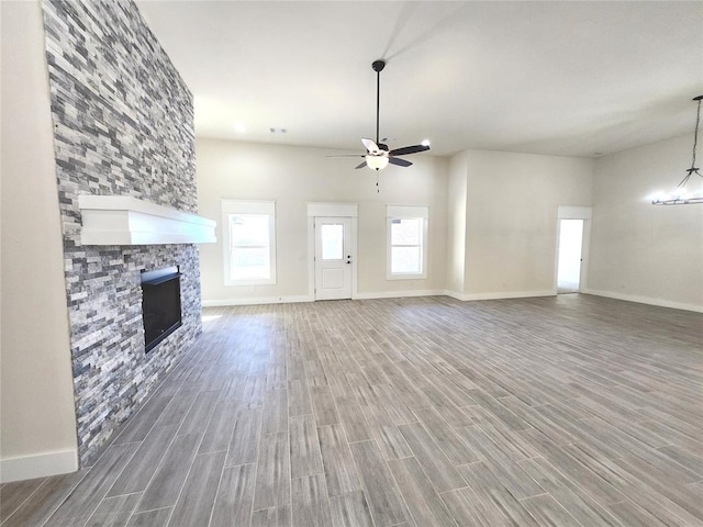 unfurnished living room with dark hardwood / wood-style flooring, a stone fireplace, and ceiling fan