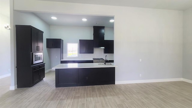 kitchen featuring stainless steel microwave, a kitchen island with sink, sink, light hardwood / wood-style flooring, and range hood