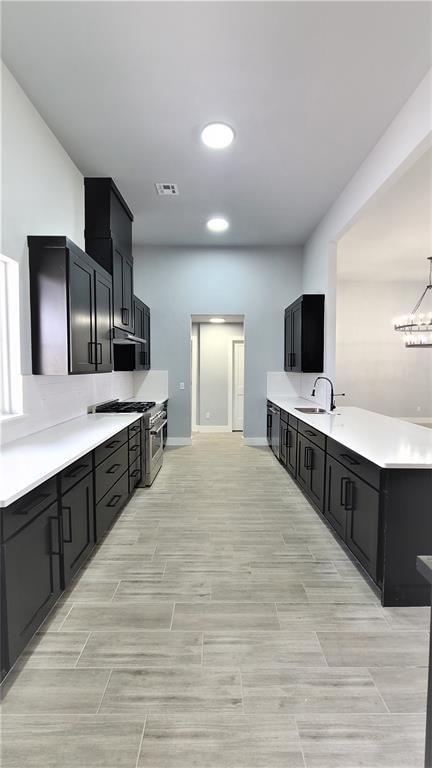 kitchen with sink, an inviting chandelier, ventilation hood, high end stove, and pendant lighting