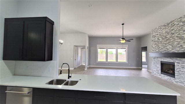 kitchen featuring ceiling fan, sink, a stone fireplace, kitchen peninsula, and light hardwood / wood-style floors