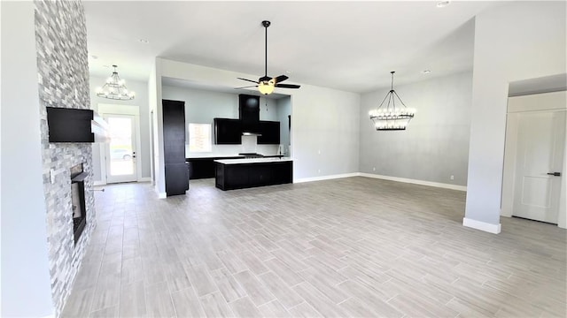 unfurnished living room with ceiling fan with notable chandelier, a stone fireplace, and light hardwood / wood-style flooring