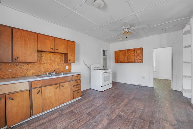 kitchen featuring dark wood-type flooring, sink, white gas range oven, decorative backsplash, and ceiling fan