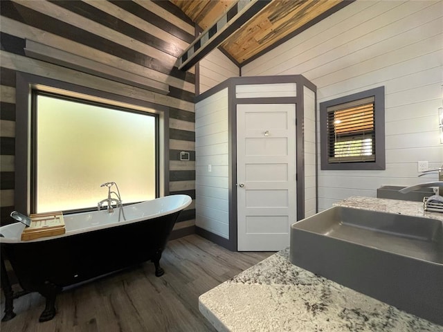 bathroom featuring a bathing tub, lofted ceiling with beams, sink, wooden walls, and hardwood / wood-style flooring