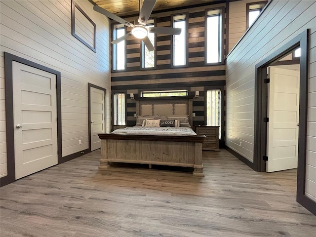 unfurnished bedroom with hardwood / wood-style floors, a towering ceiling, ceiling fan, and wooden walls