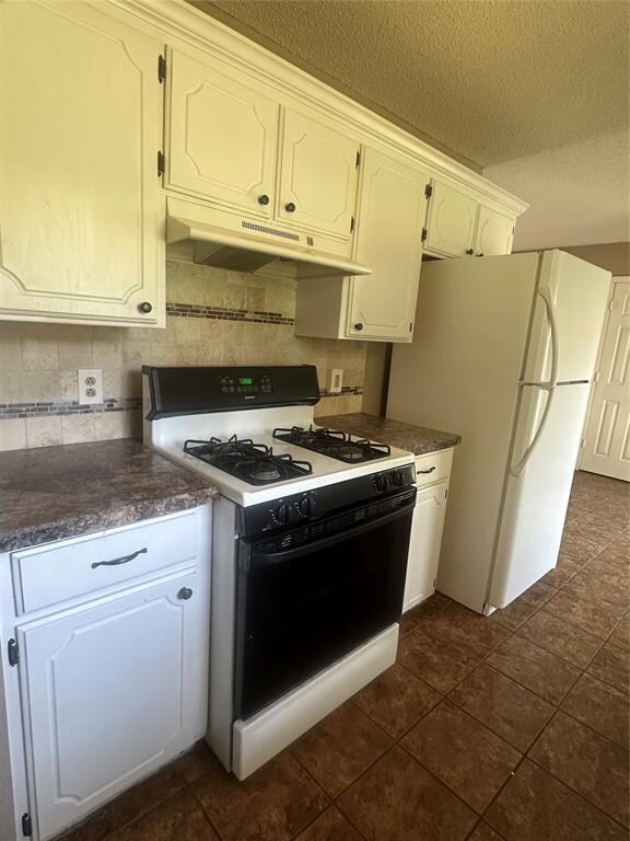 kitchen with tasteful backsplash, a textured ceiling, white appliances, dark tile patterned floors, and white cabinets