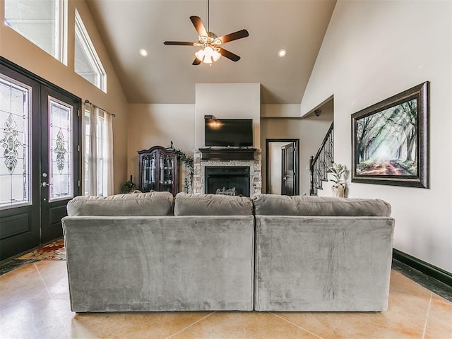 tiled living room with a stone fireplace, ceiling fan, and high vaulted ceiling