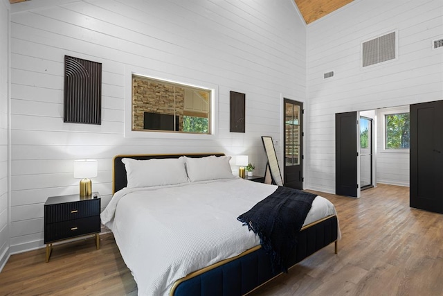 bedroom featuring wooden walls, high vaulted ceiling, and wood-type flooring