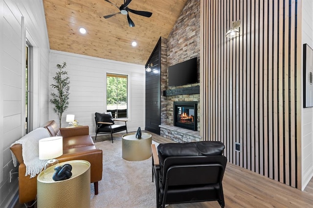 living room with wood walls, wooden ceiling, a stone fireplace, light hardwood / wood-style flooring, and ceiling fan