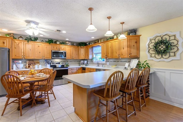 kitchen featuring pendant lighting, light tile patterned floors, a textured ceiling, appliances with stainless steel finishes, and kitchen peninsula