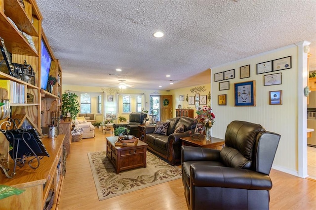 living room featuring ceiling fan, a large fireplace, light wood-type flooring, and a textured ceiling