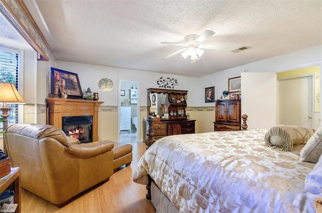 bedroom with ensuite bathroom, a textured ceiling, ceiling fan, light hardwood / wood-style flooring, and multiple windows