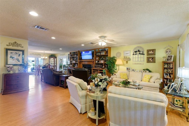 living room with ceiling fan with notable chandelier, light hardwood / wood-style floors, and a textured ceiling