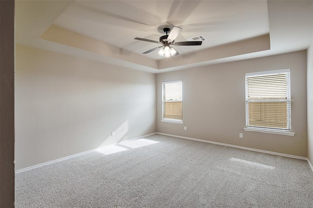 carpeted spare room with a tray ceiling, ceiling fan, and plenty of natural light