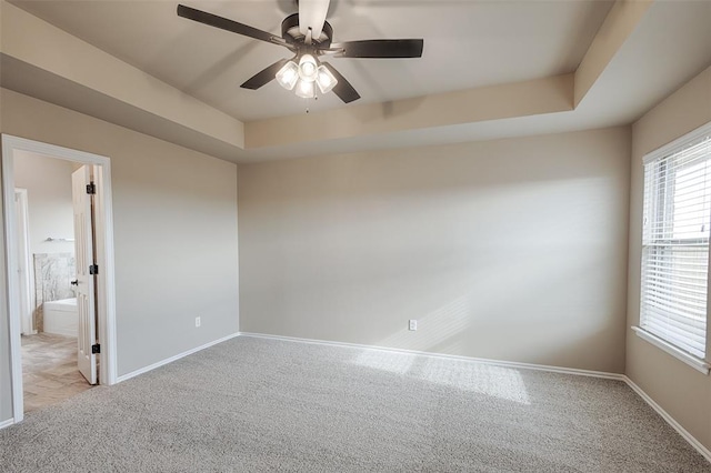 spare room featuring ceiling fan, light colored carpet, and a tray ceiling