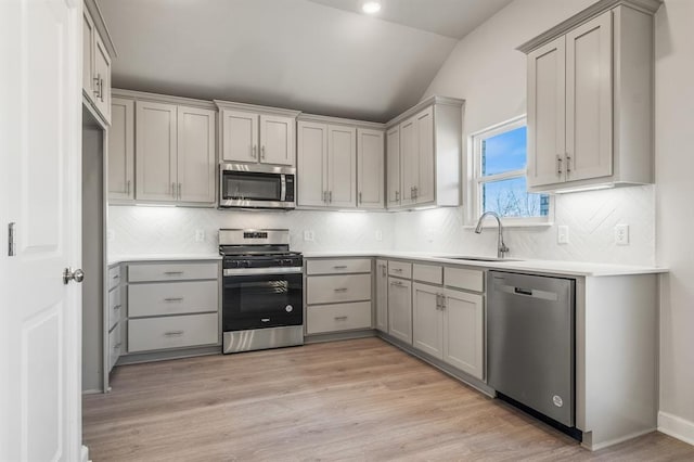 kitchen featuring decorative backsplash, appliances with stainless steel finishes, gray cabinetry, vaulted ceiling, and sink