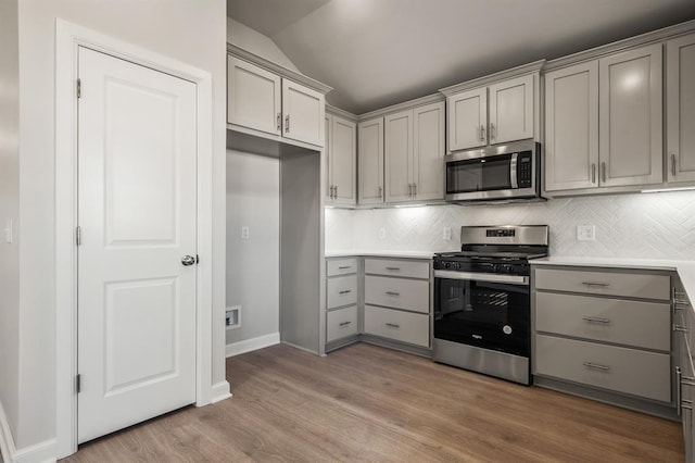 kitchen featuring appliances with stainless steel finishes, gray cabinets, light hardwood / wood-style flooring, and lofted ceiling