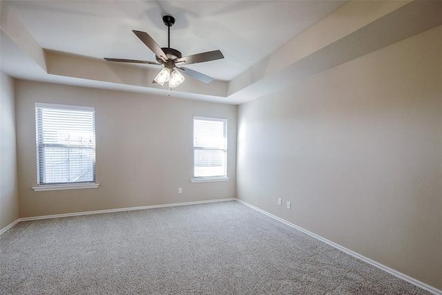 carpeted spare room with a raised ceiling and ceiling fan