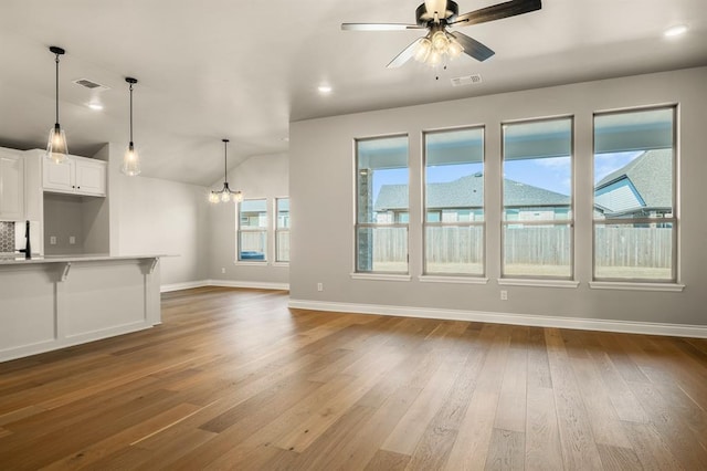 unfurnished living room featuring ceiling fan with notable chandelier, wood-type flooring, a wealth of natural light, and lofted ceiling