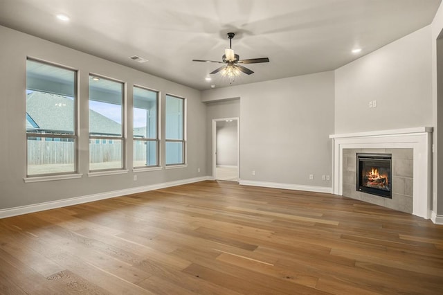 unfurnished living room featuring ceiling fan, wood-type flooring, and a tiled fireplace