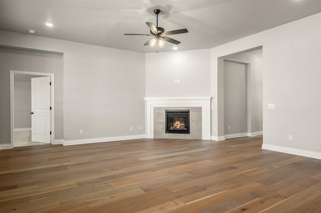 unfurnished living room featuring hardwood / wood-style flooring, ceiling fan, and a tile fireplace