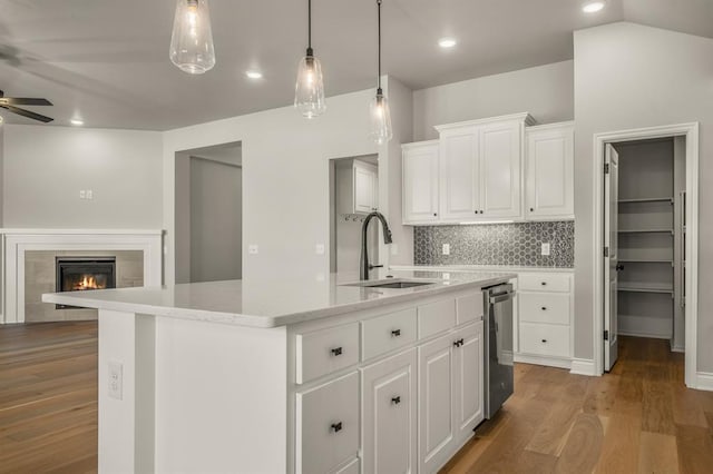 kitchen with white cabinetry, sink, wood-type flooring, a tiled fireplace, and a center island with sink