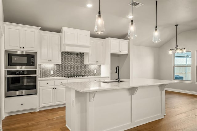 kitchen featuring appliances with stainless steel finishes, white cabinetry, a kitchen island with sink, and lofted ceiling