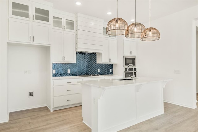 kitchen featuring appliances with stainless steel finishes, light wood-type flooring, a kitchen island with sink, sink, and decorative light fixtures