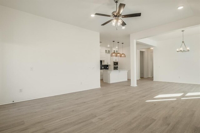 unfurnished living room with ceiling fan with notable chandelier and light hardwood / wood-style floors