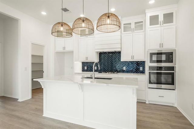 kitchen featuring pendant lighting, oven, light stone countertops, an island with sink, and black microwave