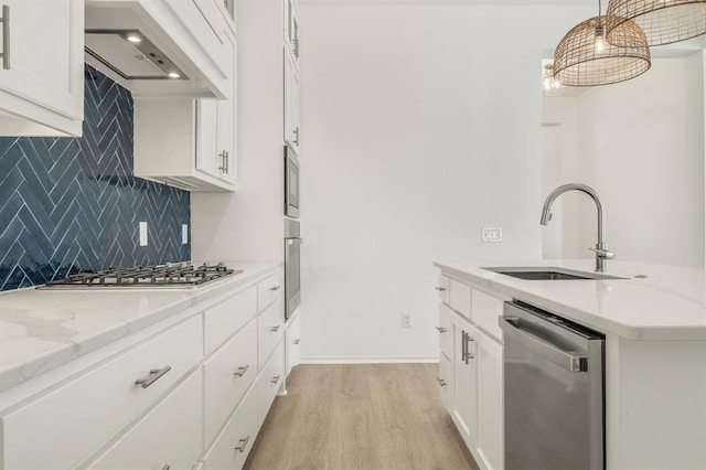 kitchen with appliances with stainless steel finishes, premium range hood, sink, white cabinets, and hanging light fixtures