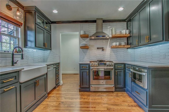 kitchen with wall chimney exhaust hood, sink, light wood-type flooring, appliances with stainless steel finishes, and decorative backsplash