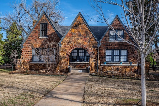 tudor home featuring a front yard, brick siding, and stone siding