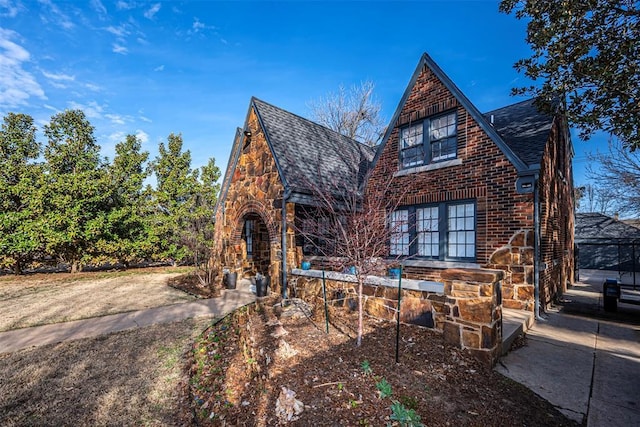 tudor-style house featuring stone siding, brick siding, and a shingled roof