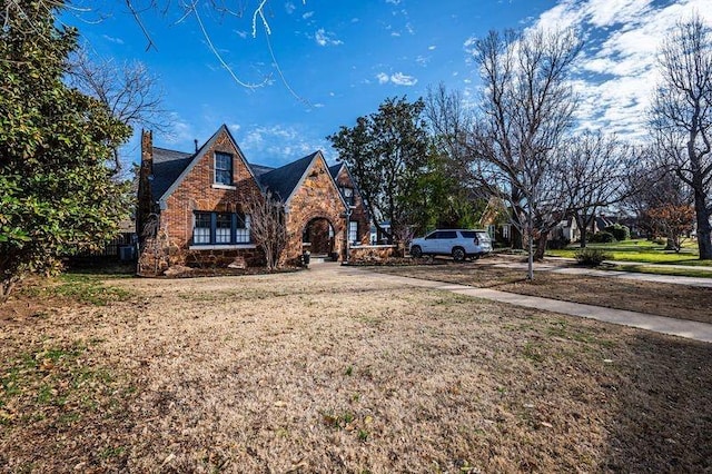 tudor-style house with a front lawn, stone siding, brick siding, and driveway