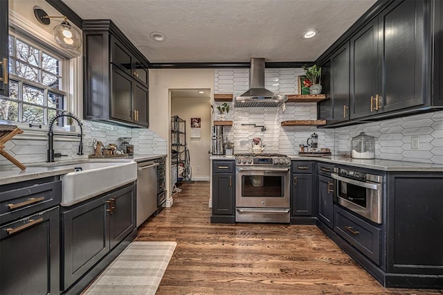 kitchen with a sink, light stone counters, dark wood finished floors, stainless steel appliances, and wall chimney exhaust hood