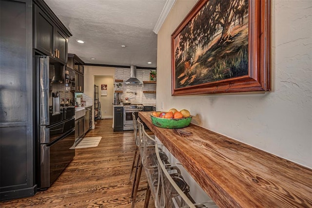 kitchen with gas range, ornamental molding, freestanding refrigerator, wall chimney exhaust hood, and dark wood-style flooring