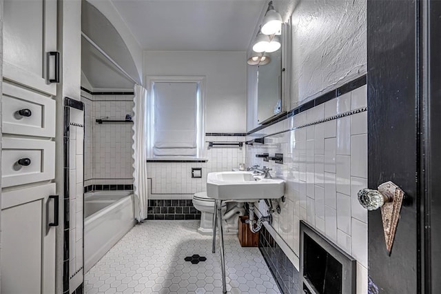 bathroom featuring tile patterned floors, shower / bath combo with shower curtain, toilet, a sink, and tile walls