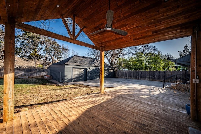 wooden deck with a fenced backyard, a garage, an outbuilding, and a ceiling fan