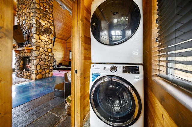 laundry room with a fireplace, stacked washing maching and dryer, and wood walls