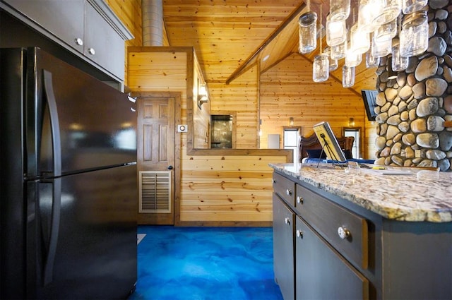 kitchen with gray cabinetry, light stone counters, fridge, wooden walls, and wood ceiling