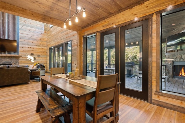 dining room with french doors, light wood-type flooring, wood ceiling, a fireplace, and wood walls