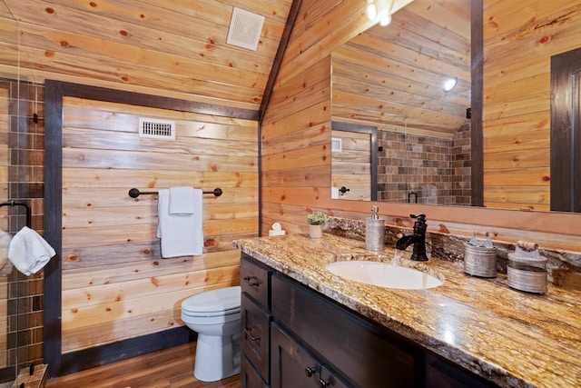 bathroom with hardwood / wood-style floors, vanity, wood walls, vaulted ceiling, and toilet