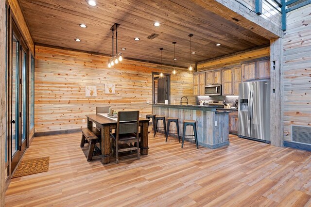 dining space featuring wood walls, light hardwood / wood-style flooring, wood ceiling, and sink